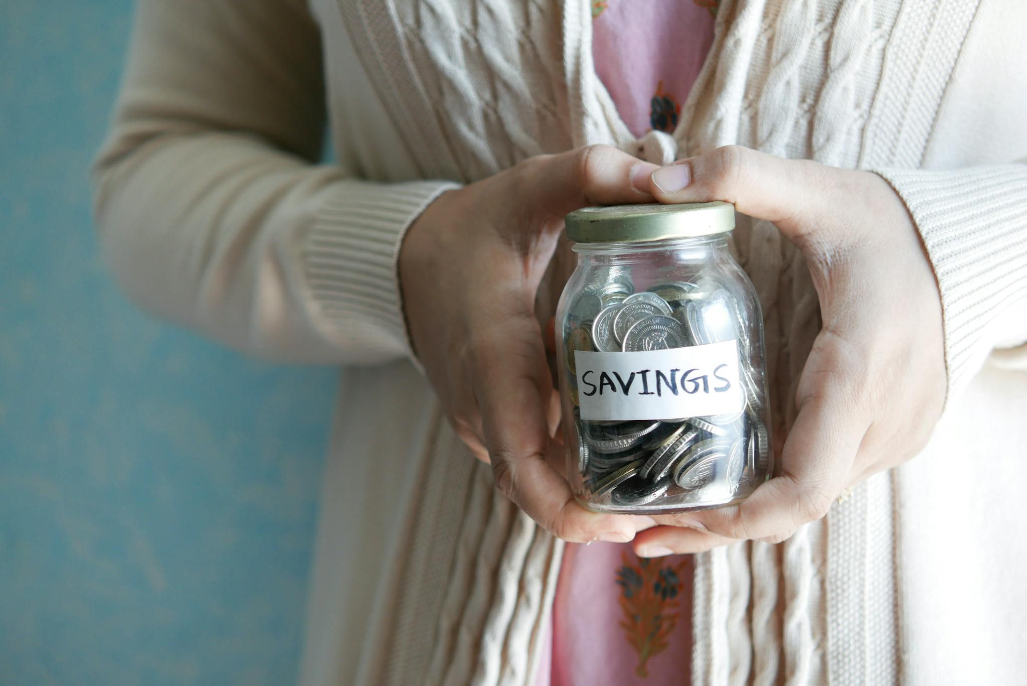 Woman holding a jar labeled 'savings' filled with coins, representing financial savings.
